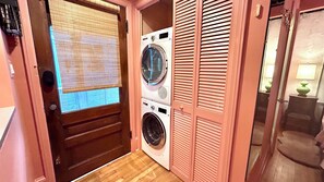 Un lavadero con lavadora y secadora, contraventanas de madera y un ventanal con persianas.