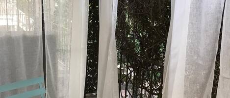 A small, round table with a single decorative item on it, situated in a covered outdoor area with white curtains and a view of greenery.