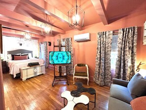 Una habitación con una cama, televisión, una silla, un sofá y piso de madera.