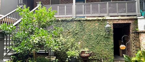 A covered outdoor area with a brick wall, a metal railing, and potted plants.