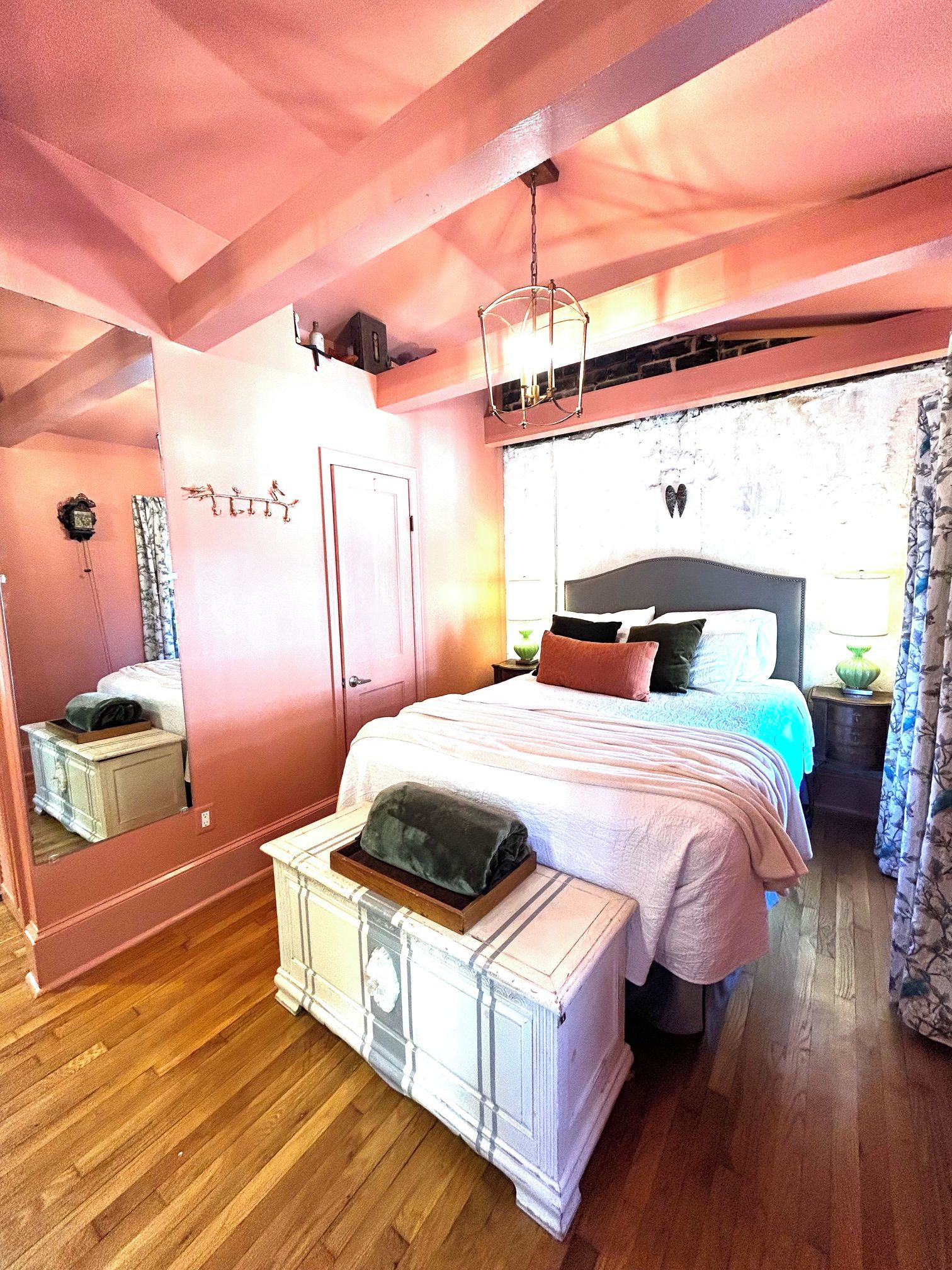 A bedroom with a bed, bedside tables, a dresser, a mirror, and a hanging light fixture.