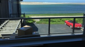 A view from a balcony overlooking a beach with a red convertible parked in the foreground.