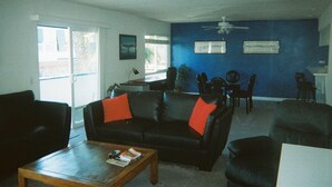 A living room with a black leather sofa, a wooden coffee table, and a dining area with a table and chairs. - Seashore Dr - 12 Bikes, 10 Boards, 8 Wetsuits, 11 Beach Chairs & Beach Toys - (Newport Beach)