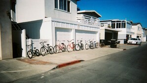 A row of bicycles parked along a sidewalk next to a white building with a garage. - Seashore Dr - 12 Bikes, 10 Boards, 8 Wetsuits, 11 Beach Chairs & Beach Toys - (Newport Beach)