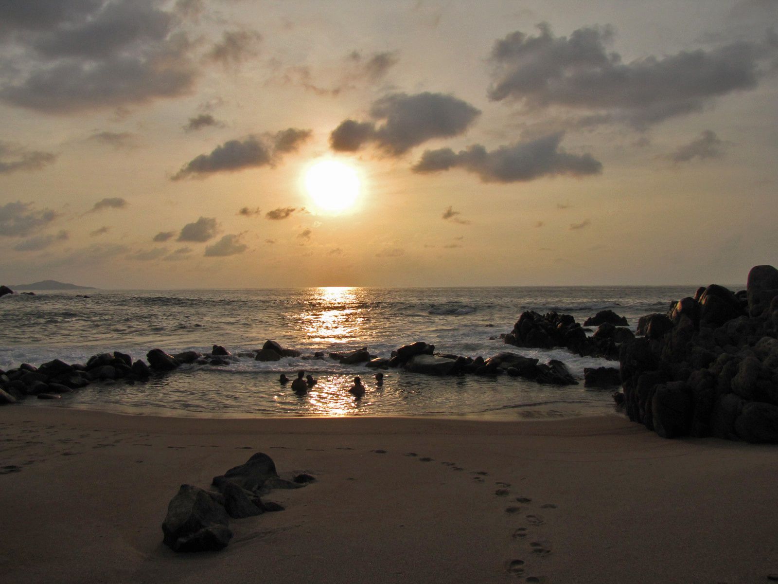 A beach with rocks and footprints leading to the water.