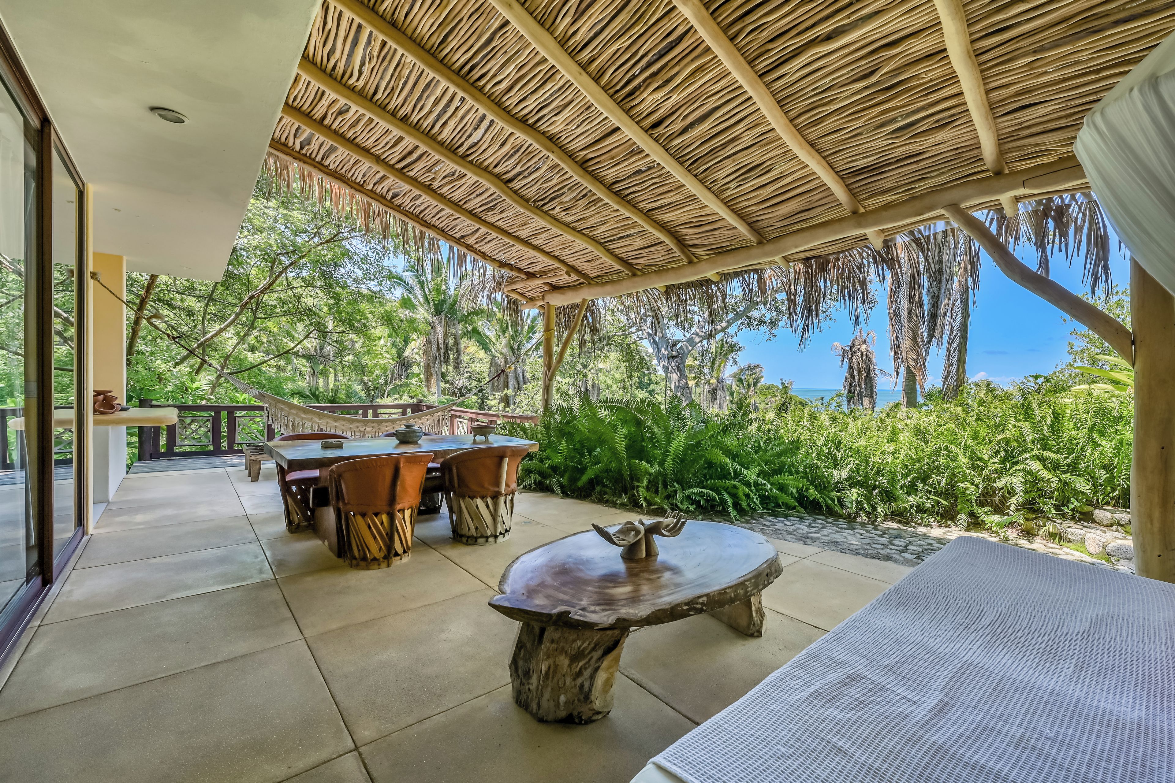 An outdoor patio with a thatched roof, a round wooden table, and a dining table with chairs.