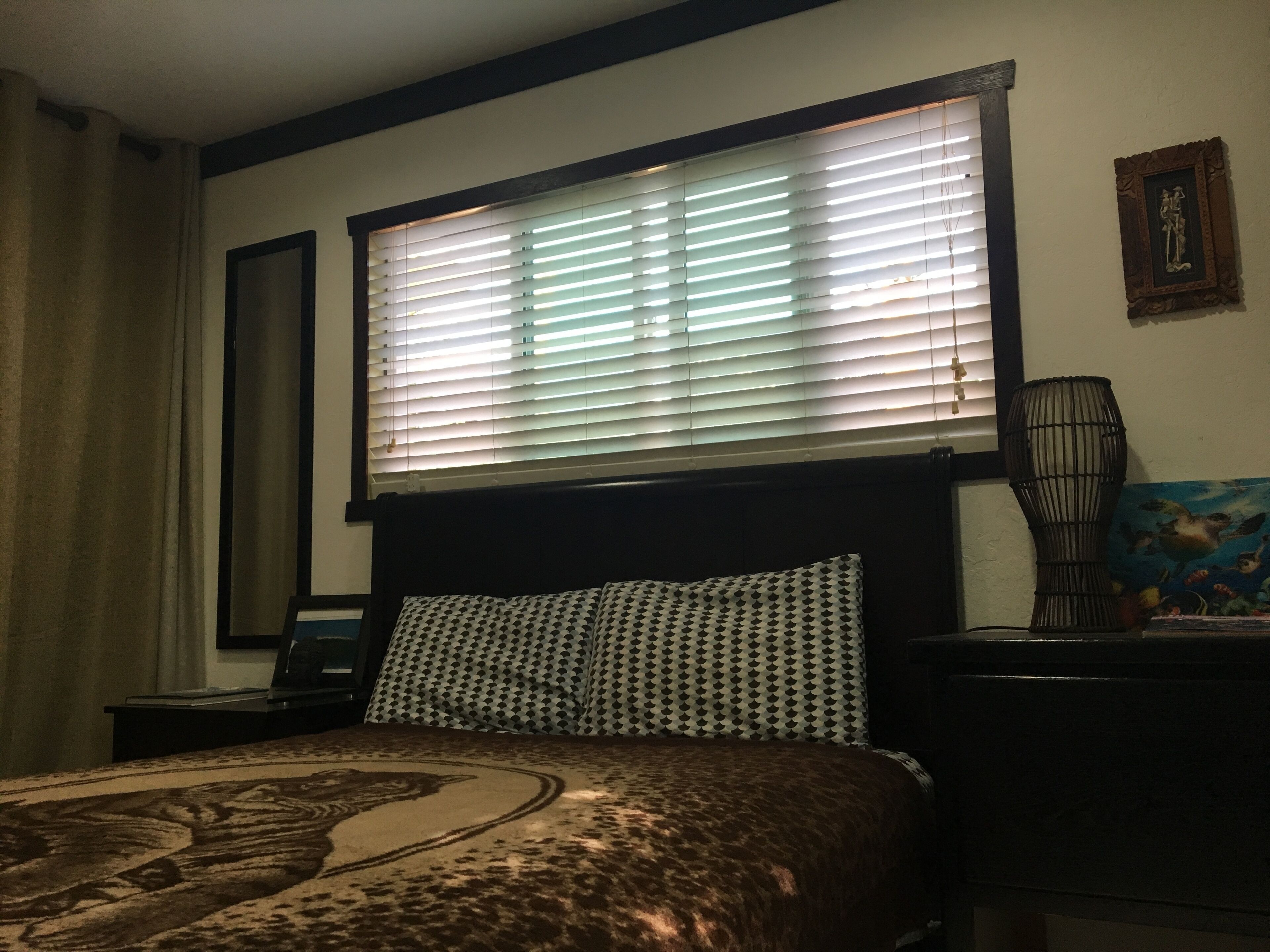 A bedroom with a bed, a nightstand, a lamp, and a window with blinds.