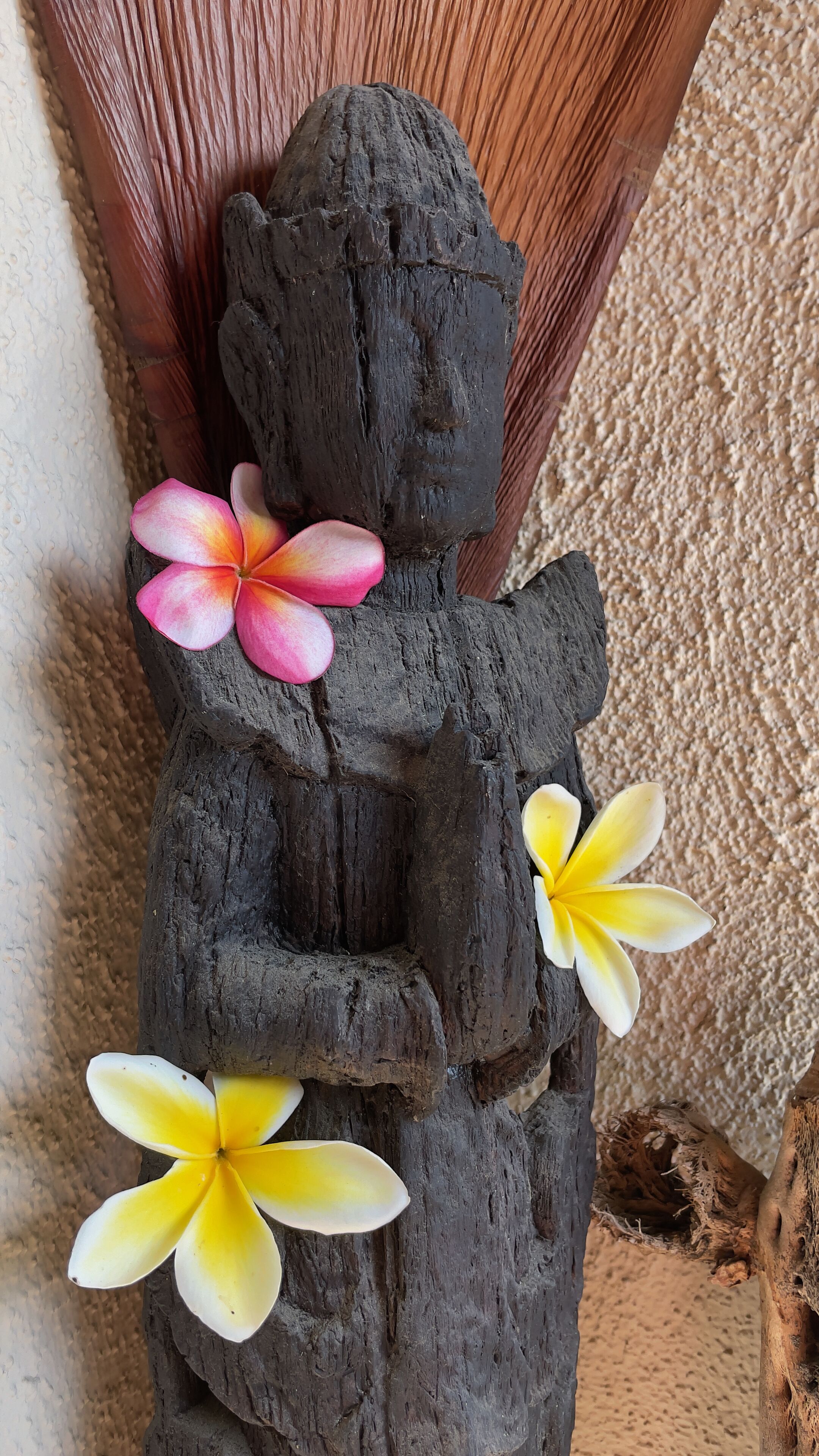 A dark wooden sculpture with two flowers, one pink and one yellow, placed on it.