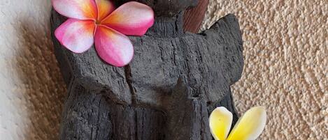 A dark wooden sculpture with two flowers, one pink and one yellow, placed on it.