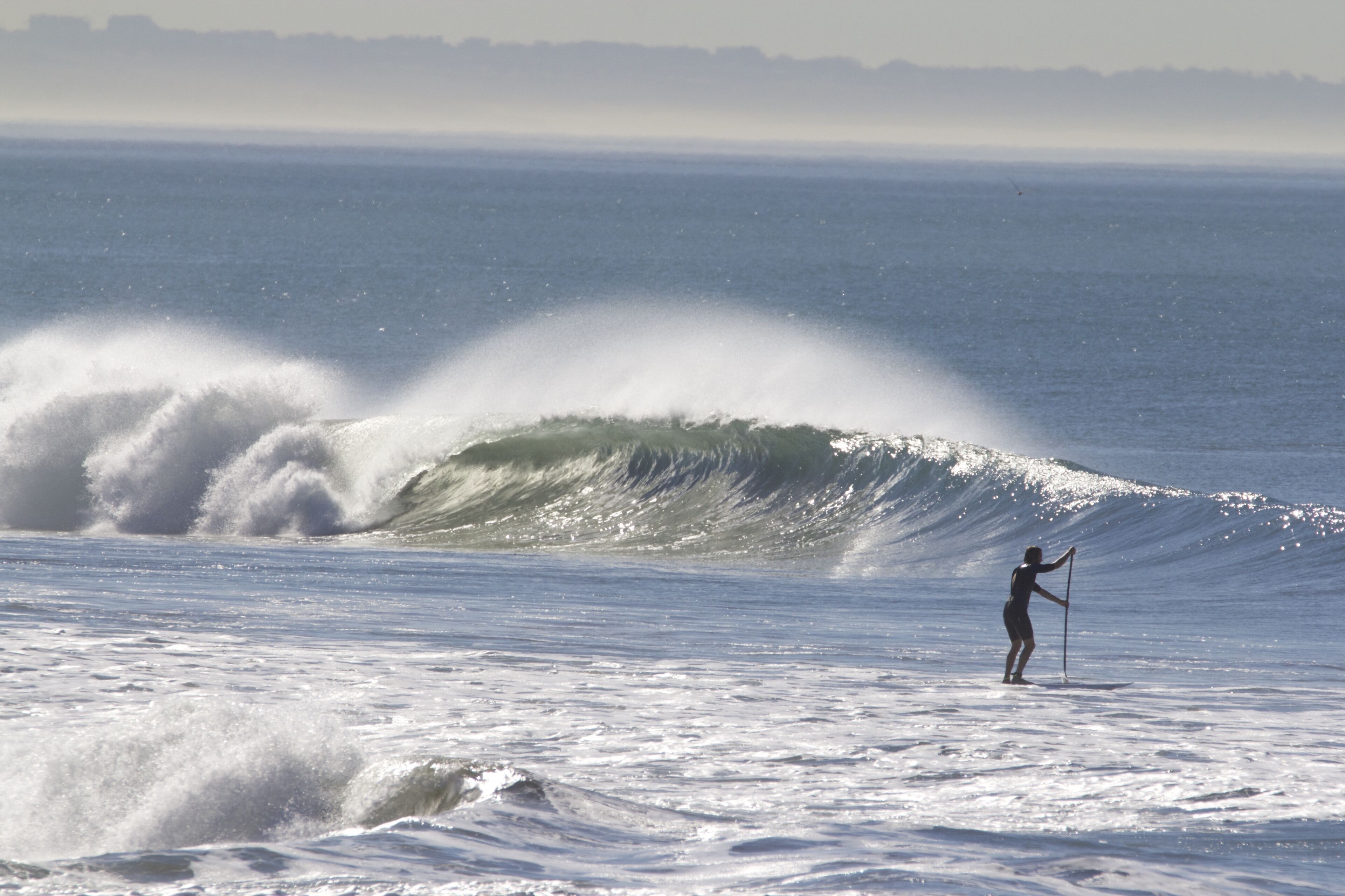 A person paddleboarding on a wave with a clear view of the ocean and distant shoreline.