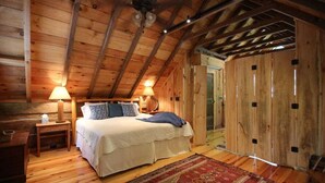Un dormitorio de cabaña de madera con una cama, lámparas de noche, una mesita de noche y una alfombra estampada.