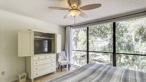 Une chambre à coucher avec un grand lit, une armoire, une chaise et un ventilateur de plafond.