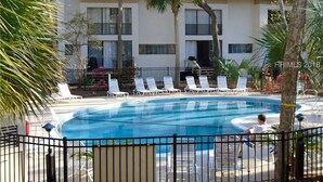 Une piscine entourée de chaises longues, de palmiers et d’un bâtiment doté de nombreuses fenêtres.