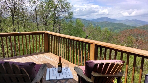 A wooden deck with a table and chairs, overlooking a mountainous landscape.