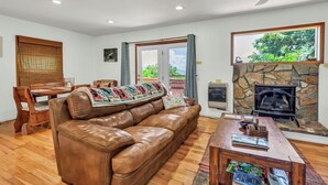 A cozy living room with a leather sofa, wooden coffee table, stone fireplace, and a dining area with a wooden table and chairs.