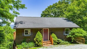 A two-story house with a front porch, a red door, and a small front yard.