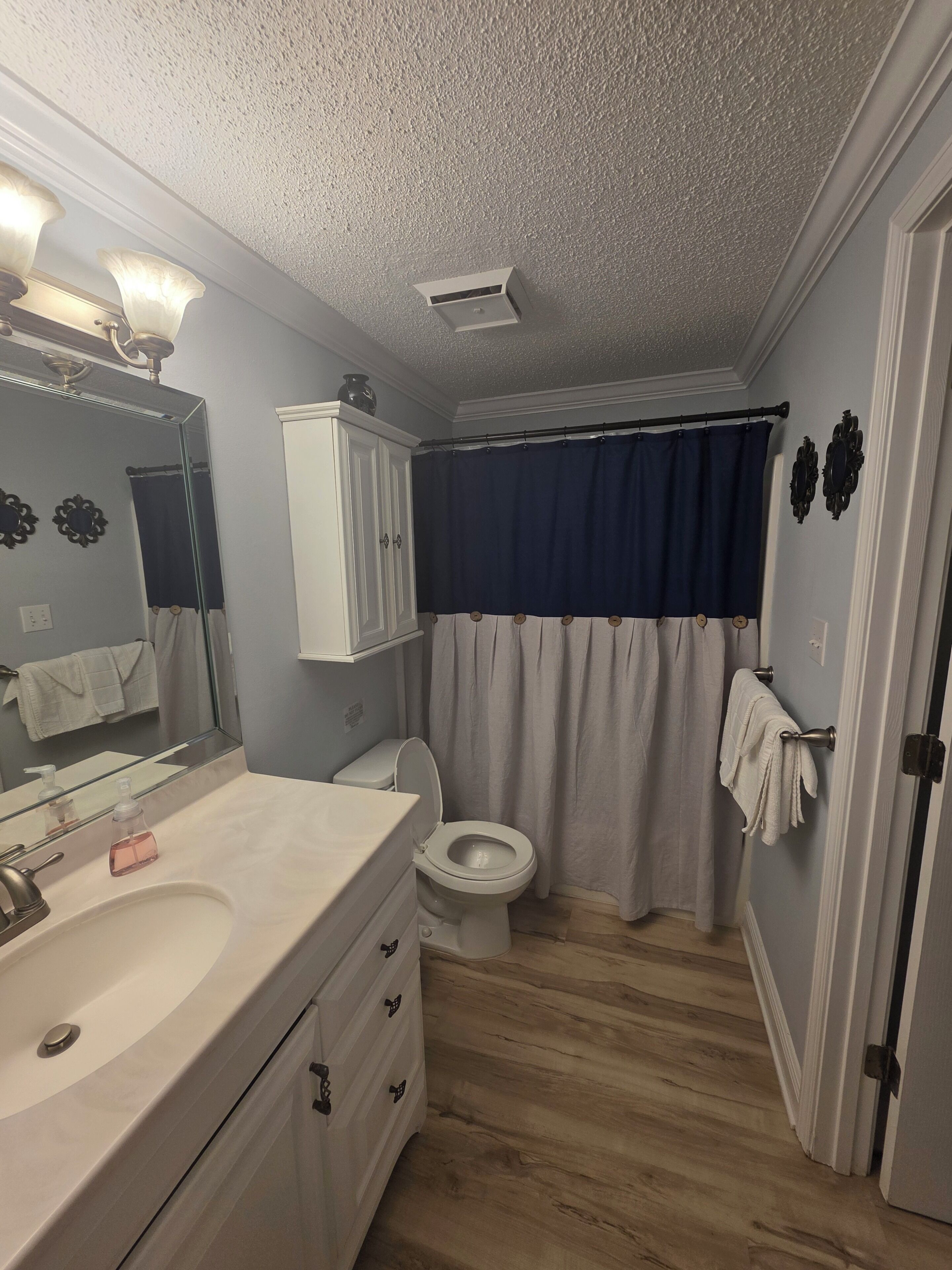 Une salle de bain avec un lavabo blanc, des toilettes, un miroir et un rideau de douche.
