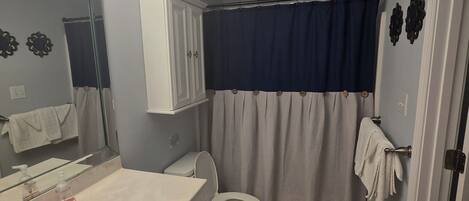 Une salle de bain avec un lavabo blanc, des toilettes, un miroir et un rideau de douche.