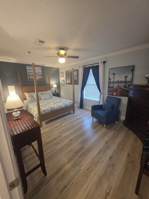 A bedroom with a four-poster bed, a desk with a lamp, a chair, a dresser, and a ceiling fan. - Ground floor! Private Balcony!
Beautifully located!! 1 bedroom
3 Sleeping Areas (Destin)