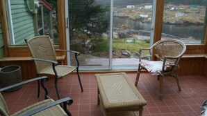 A covered patio with wicker furniture and a view of a lake and buildings. - Experience Peace And Tranquility At Charming Cottage In Small Fishing Community. (Trinity T.B.)