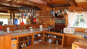 A wooden kitchen with hanging pots, a microwave, and various kitchen utensils. - Experience Peace And Tranquility At Charming Cottage In Small Fishing Community. (Trinity T.B.)