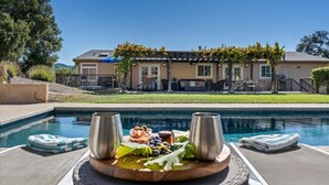 Ein Poolbereich mit Holztisch für zwei Personen, einem Pool und einem Haus im Hintergrund.