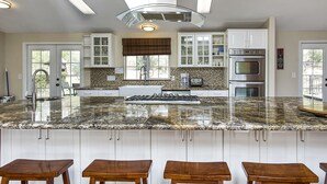 Eine moderne Küche mit Granit-Arbeitsplatten, weißen Schränken und einer zentralen Kochinsel mit Hockern.