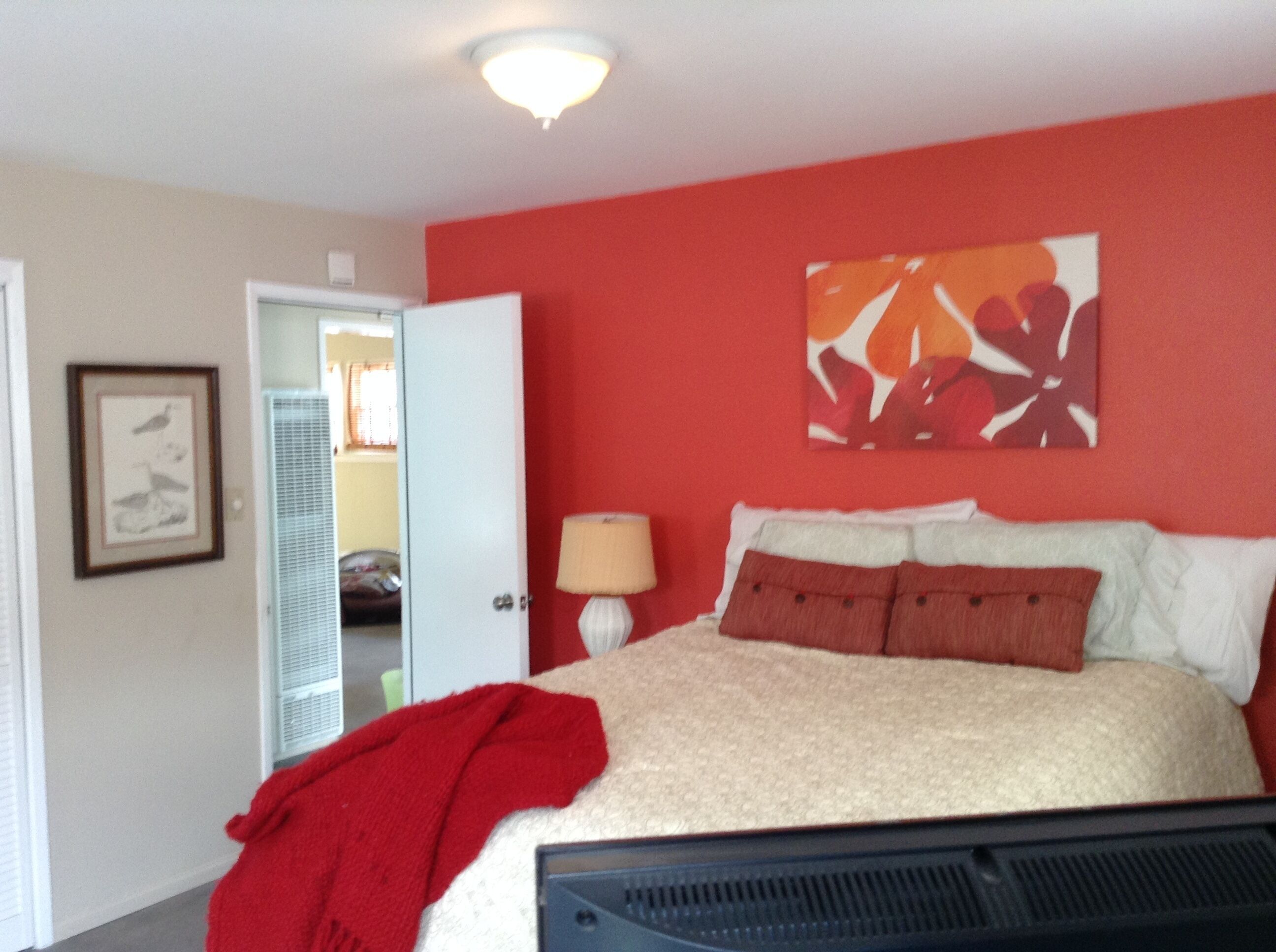 Un dormitorio con una cama, una pared roja, una puerta y un cuadro enmarcado.