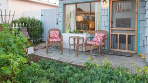 Eine Terrasse mit Korbstühlen und einem Tisch, eine Holztür und ein Fenster mit Vorhängen.