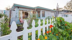 Ein Haus mit weißem Zaun, einer Veranda mit einem Stuhl und einem Garten mit verschiedenen Pflanzen und Blumen.