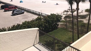Une vue sur la plage depuis un balcon, avec des voitures garées, une clôture et des palmiers.