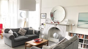 A living room with two grey sofas, a wooden coffee table, a fireplace with a mirror above it, and a bookshelf filled with books.