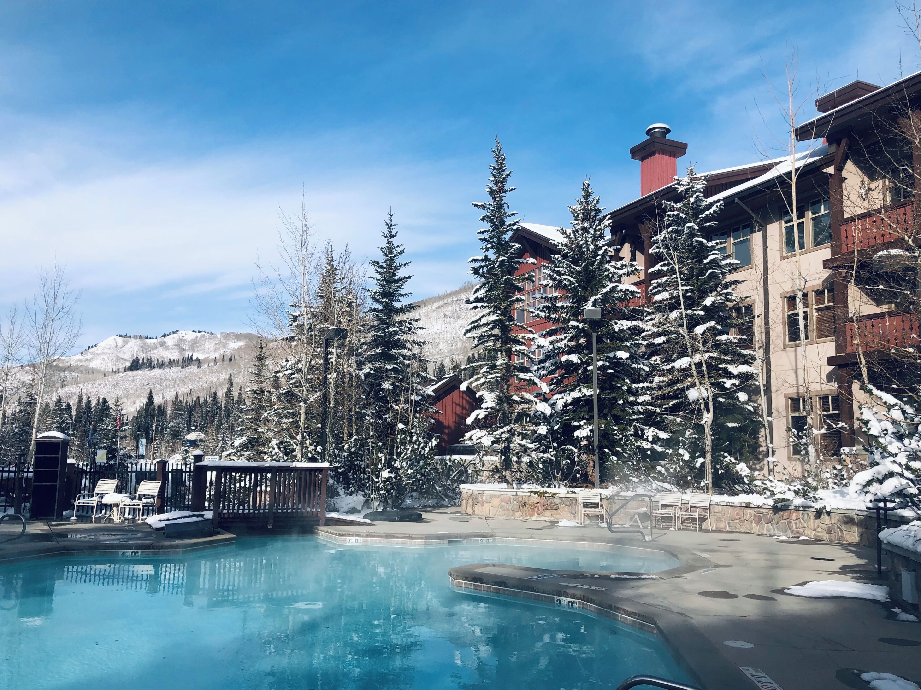 A resort with a swimming pool, snow-covered trees, and a mountain backdrop.