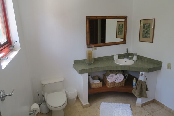 A bathroom with a toilet, sink, mirror, and a window.