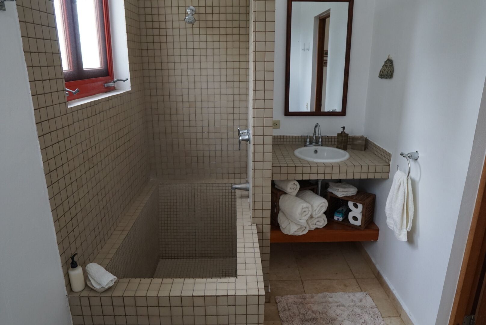 Un baño con ducha azulejada, lavamanos y espejo.