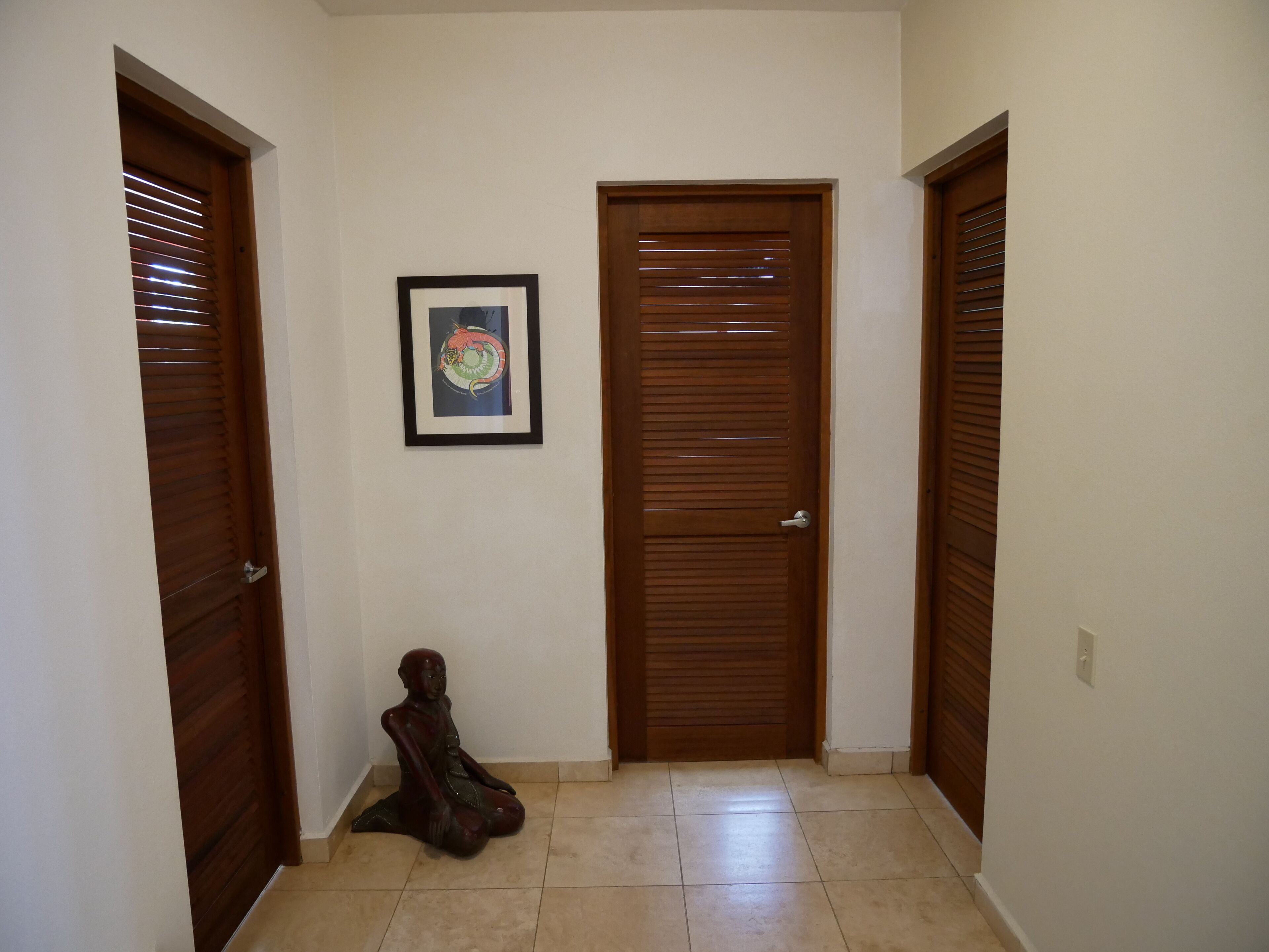 A hallway with wooden doors, a framed picture on the wall, and a sculpture on the floor.