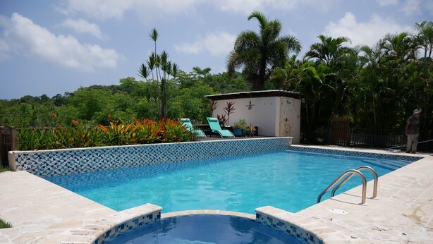 Ein Schwimmbecken mit Fliesenrand, ein Whirlpool und eine Lounge-Bereich mit Stühlen.