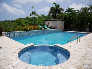 A swimming pool with a tiled edge, a hot tub, and a lounge area with chairs.