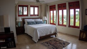 Ein Schlafzimmer mit einem Bett, zwei Nachttischlampen, einem Deckenventilator und großen Fenstern mit roten Rahmen.