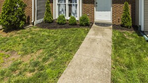 A two-story townhouse with a brick facade, a front door, and a small front yard with a pathway leading to the entrance. - A Renovated 3 Bedroom, 2.5 Bath Townhouse In Downtown Lexington. (Lexington)