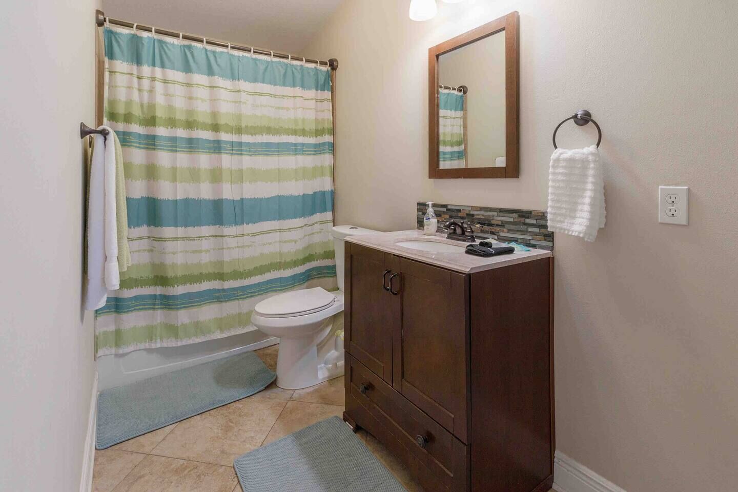 A bathroom with a striped shower curtain, a toilet, a sink with a mirror above it, and a towel rack.