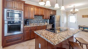 Una cocina moderna con armarios de madera, electrodomésticos de acero inoxidable, encimera de granito e iluminación colgante.