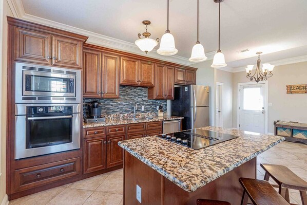 A modern kitchen with wooden cabinets, stainless steel appliances, a granite countertop, and pendant lighting.