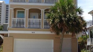 Un edificio residencial de dos pisos con garaje, balcones y una palmera en el jardín delantero.