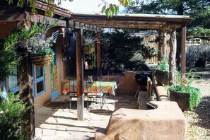 A patio with a table and chairs, a grill, and hanging plants.