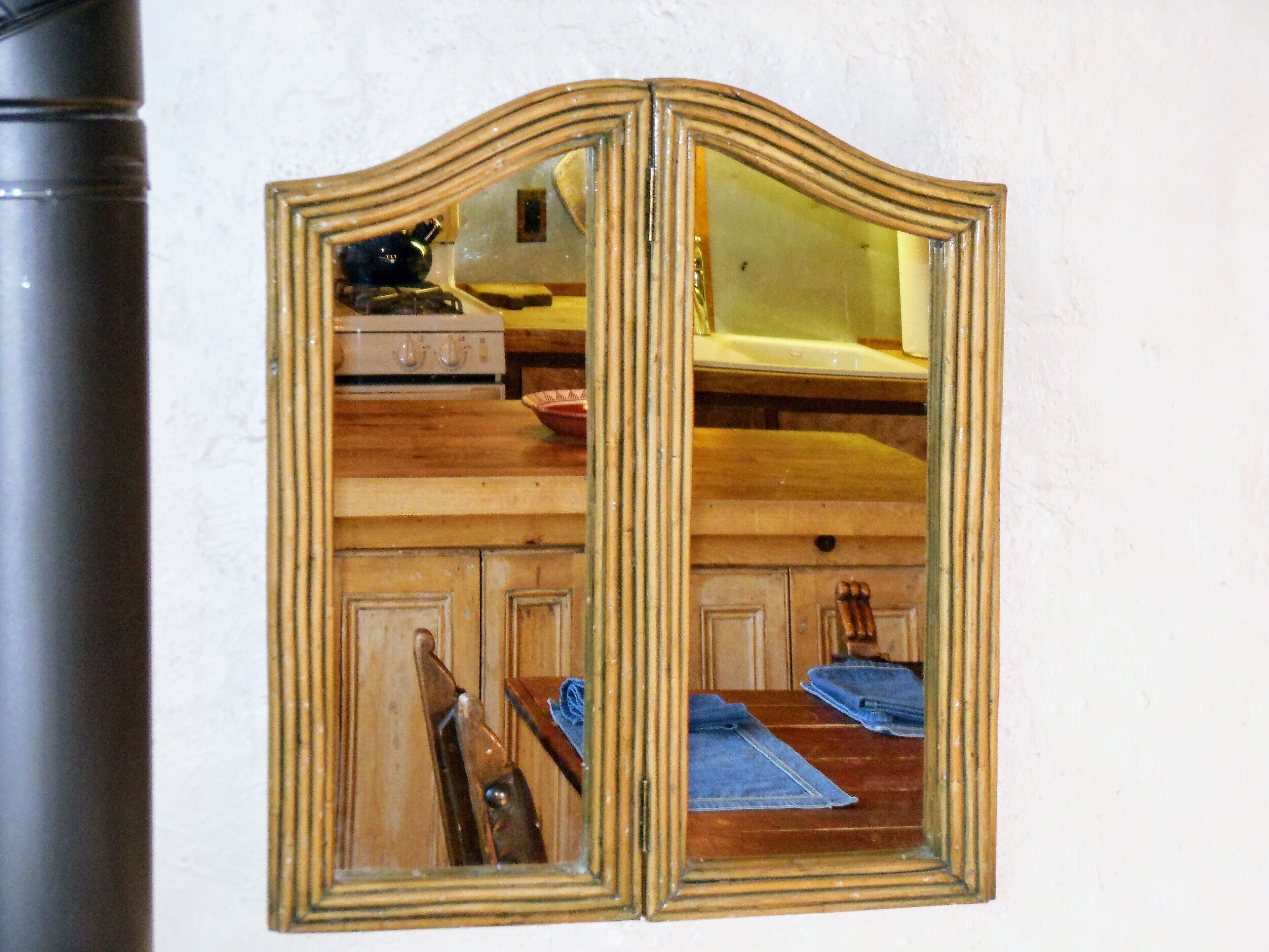 A mirror with a wooden frame reflecting a kitchen area with a stove, cabinets, and a chair.