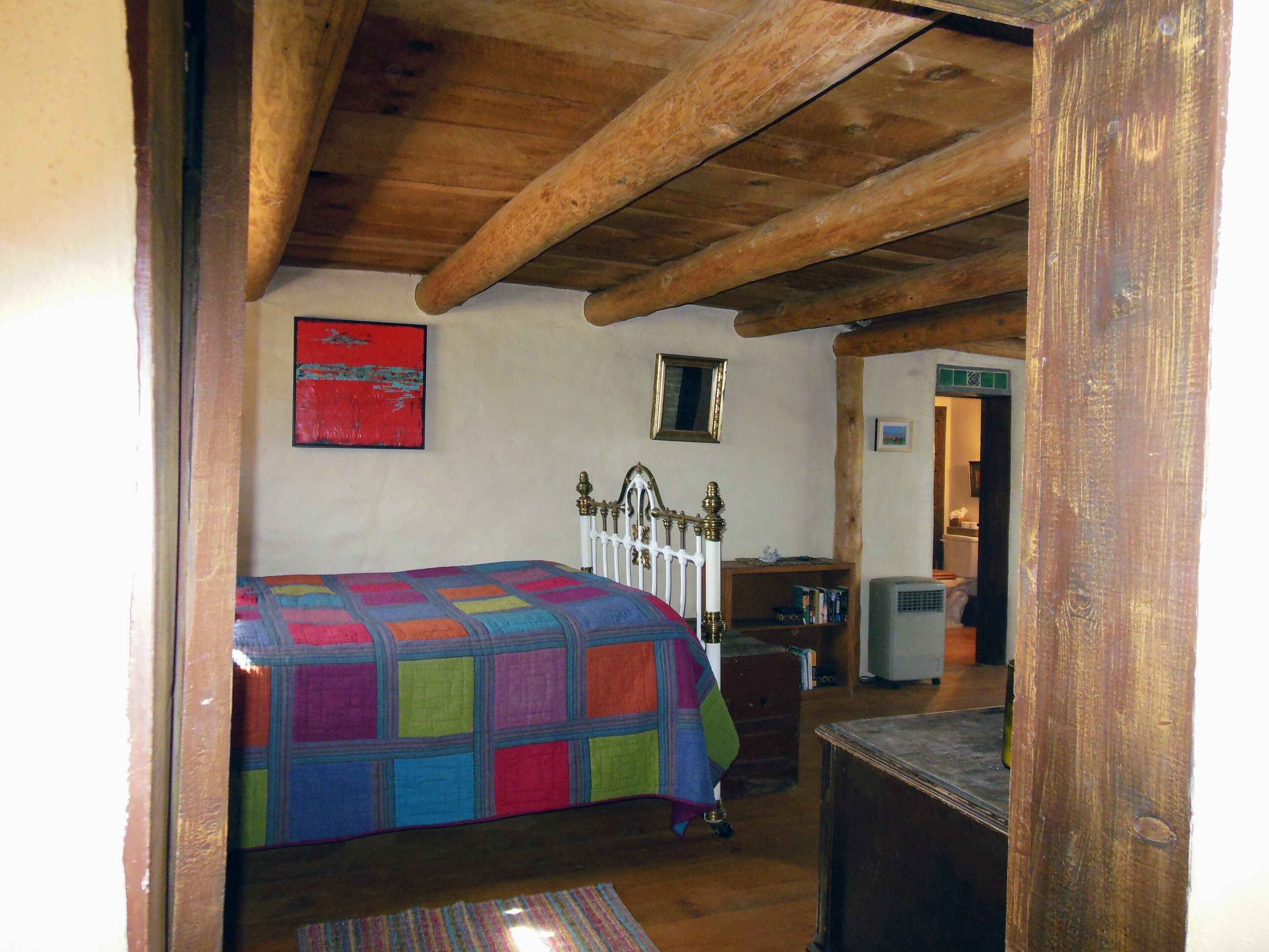 A bedroom with a wooden ceiling, a bed with a colorful quilt, a dresser, and a mirror on the wall.
