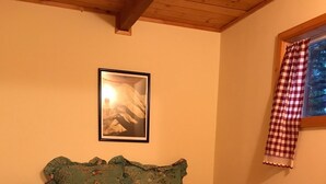 Une chambre à coucher avec un lit, une table de chevet, une lampe, un tableau encadré au mur et une fenêtre avec un rideau à carreaux.
