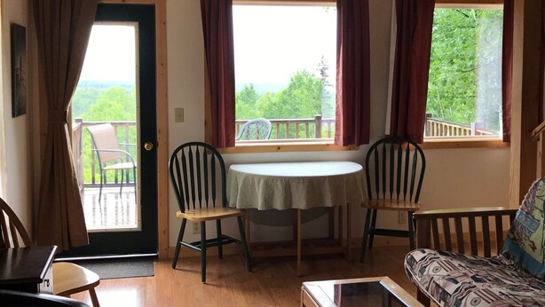 Une pièce chaleureuse avec un plafond en bois, une table à manger avec deux chaises, un canapé et une fenêtre avec des rideaux.