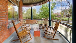 A covered porch with wooden rocking chairs and a bench, brick walls, and a view of the surrounding area. - Queen Ann Historic Mansion (Covington)